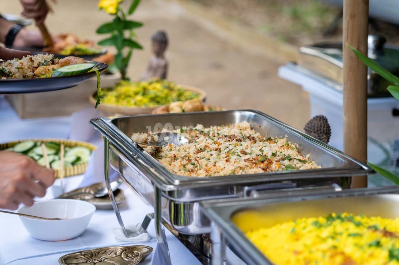 Buffet avec plats variés, notamment du riz sauté, du riz jaune et des légumes, présenté sur une table en extérieur.