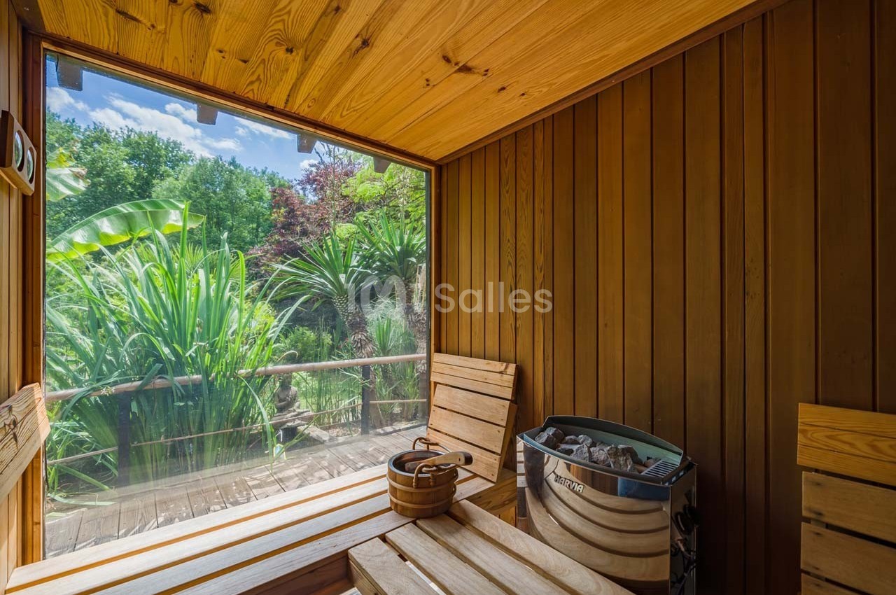 Vue intérieure d'un sauna en bois avec une grande fenêtre donnant sur un jardin luxuriant et ensoleillé.