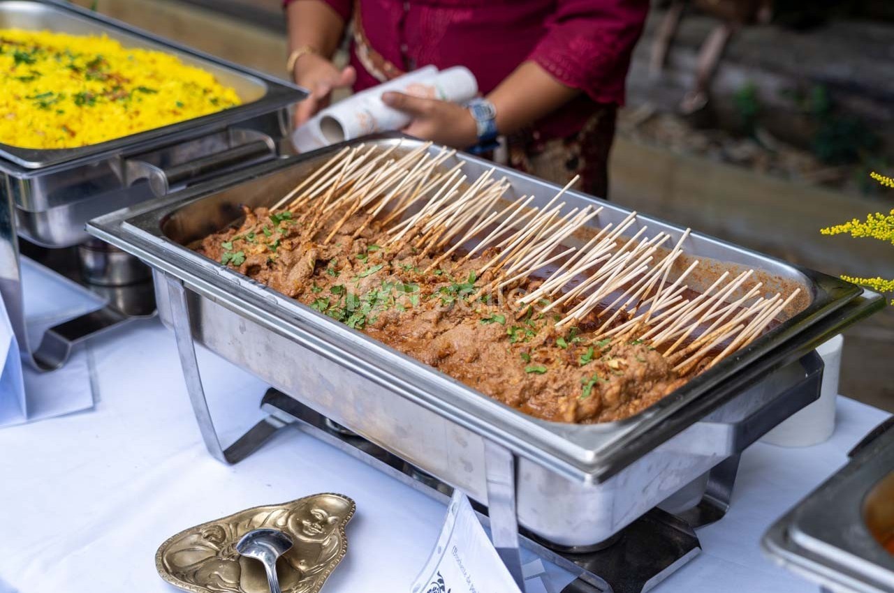 Brochettes de viande grillée servies dans un plat en inox, accompagnées de riz jaune en arrière-plan.