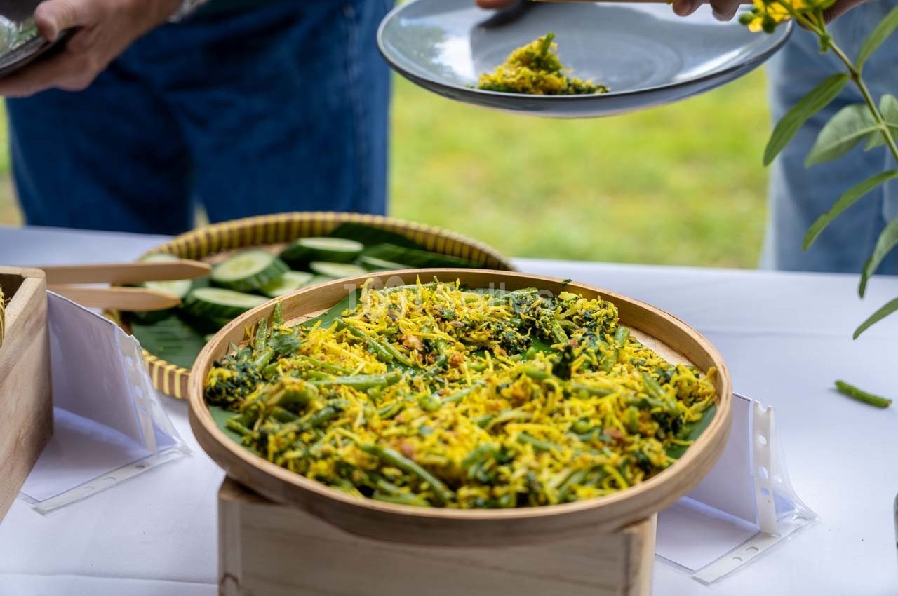 Un plat de salade colorée à base de légumes et d'herbes est servi dans un panier en bambou sur une table blanche.