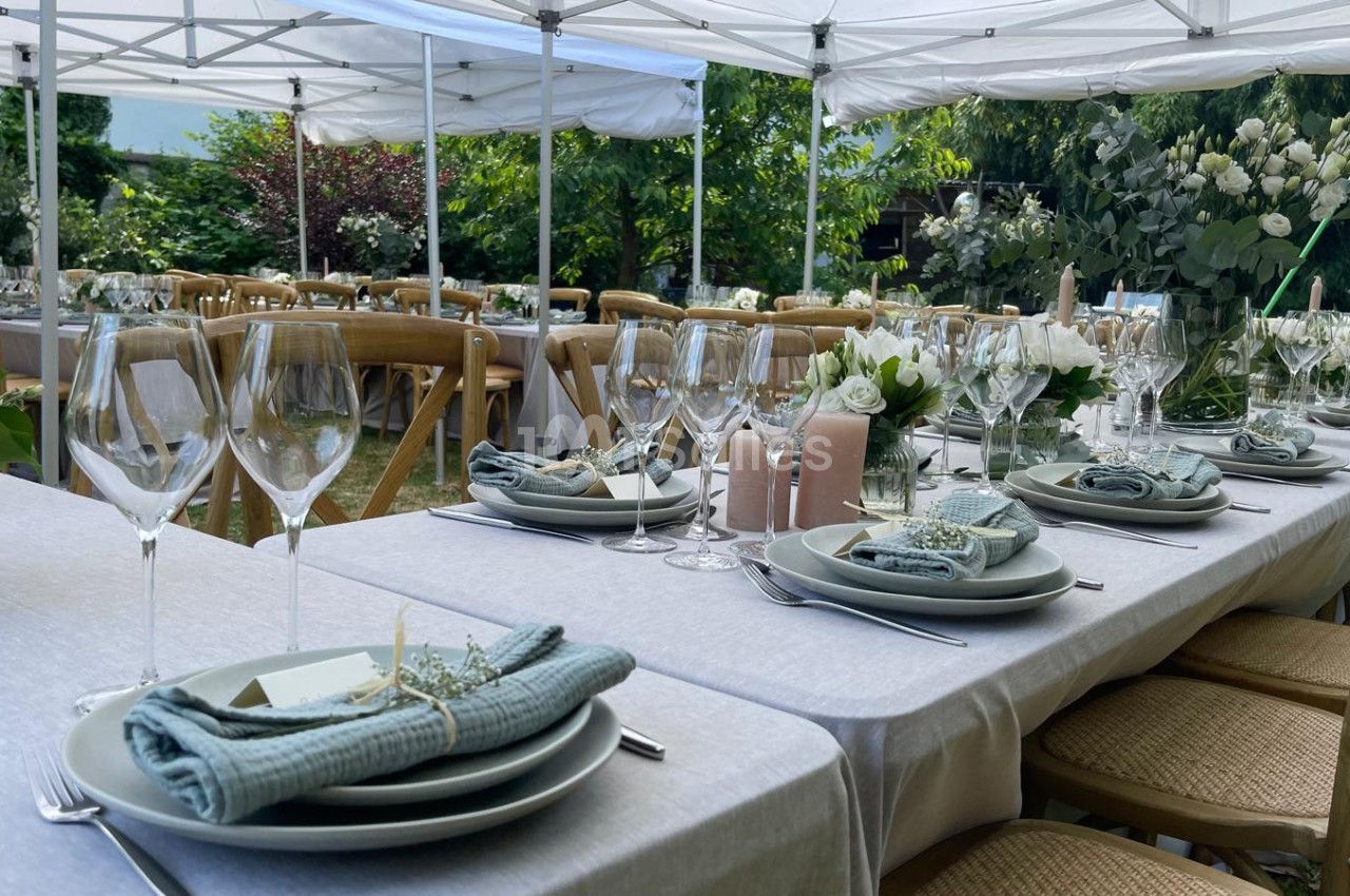 Tables dressées avec nappes blanches, vaisselle élégante, verres à pied et décorations florales sous des tonnelles…