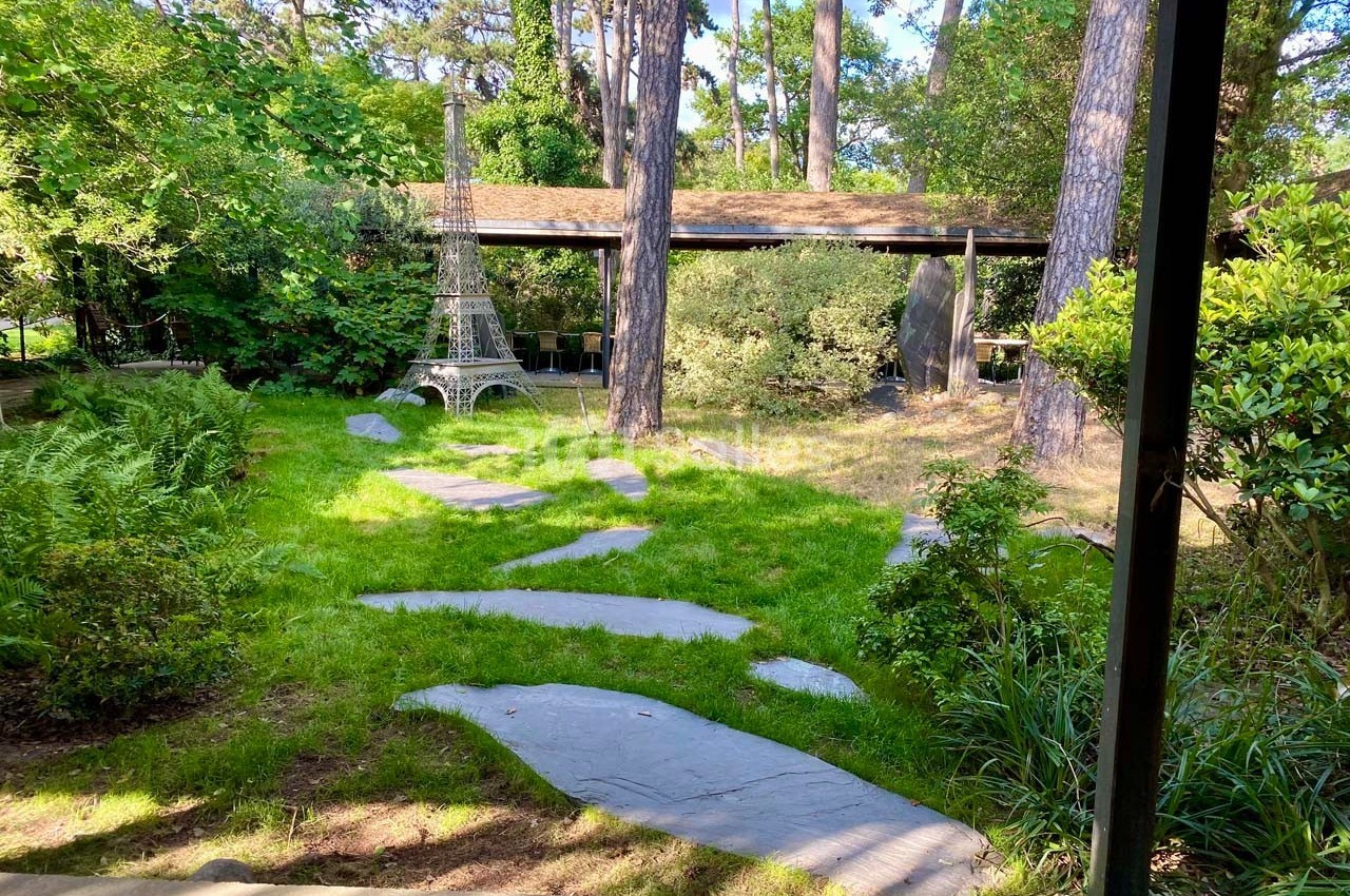 Jardin verdoyant avec des arbres, un sentier en pierres et une petite réplique de la tour Eiffel en métal.