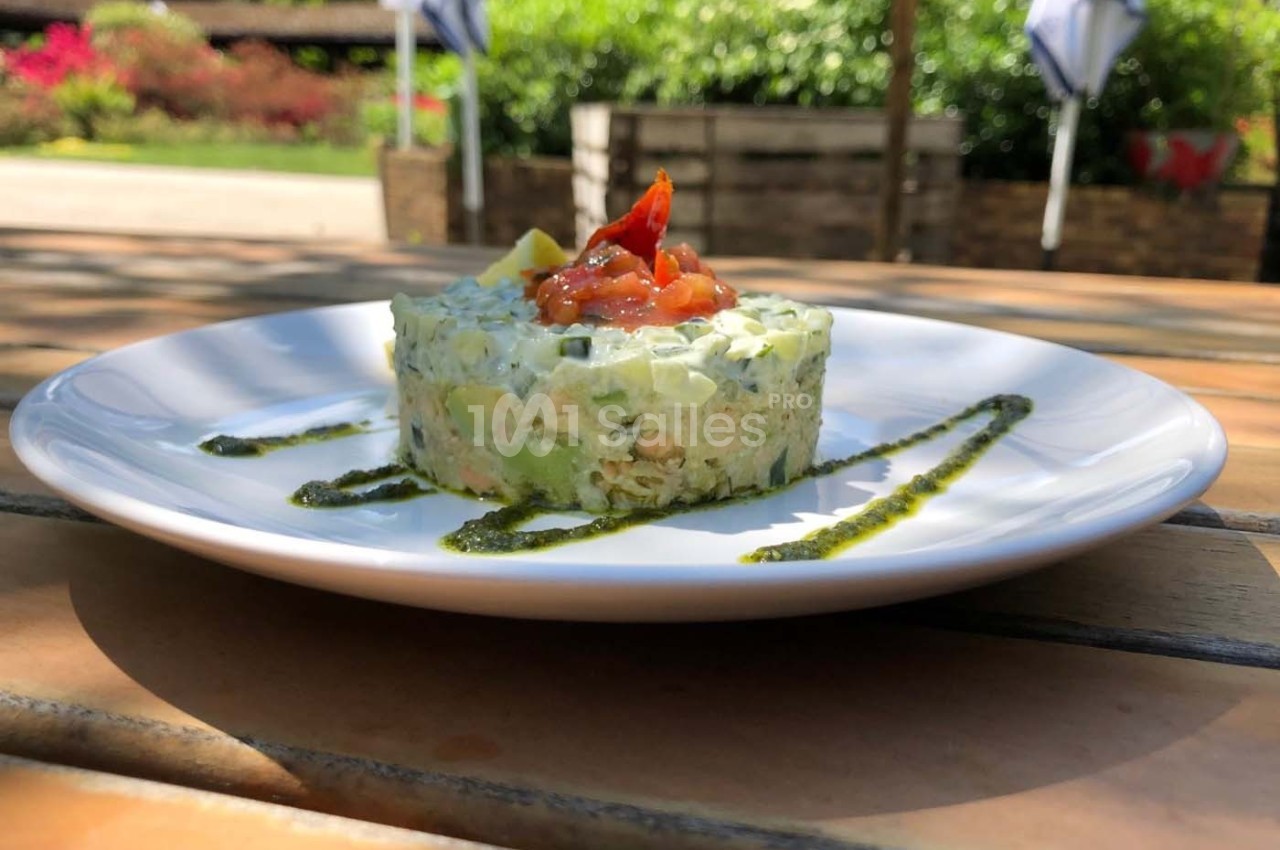 Tartare de légumes frais avec une garniture de tomates et avocat, servi sur une assiette blanche en extérieur.