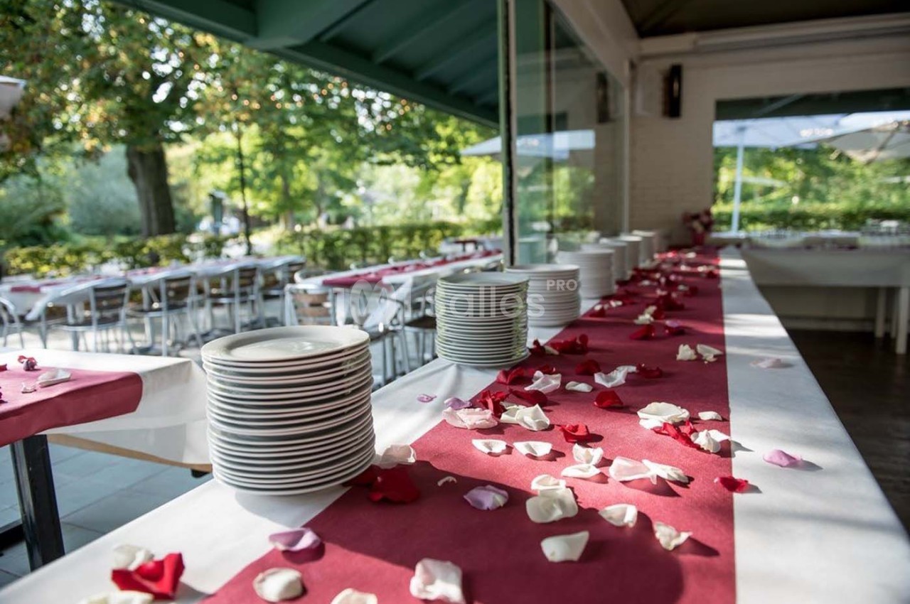 Empilement d'assiettes sur une table décorée de pétales de roses, dans une salle lumineuse avec vue sur un jardin.