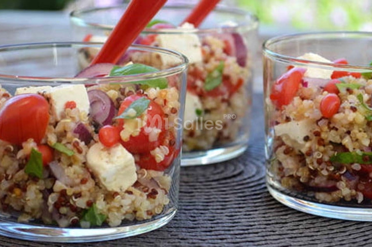 Verrines de salade de quinoa garnies de tomates cerises, feta, oignons rouges et herbes fraîches, avec des cuillères rouges.