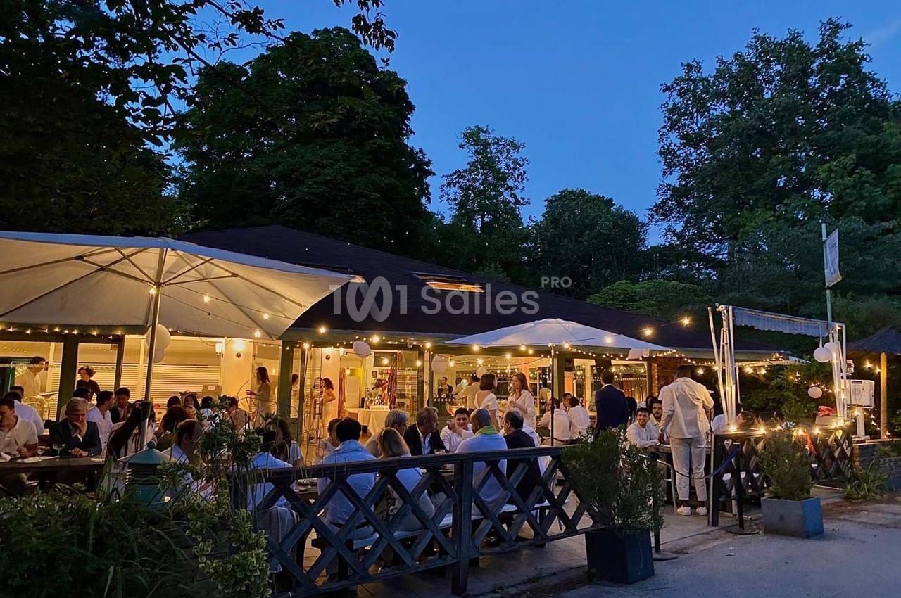 Terrasse d'un restaurant en soirée, éclairée par des guirlandes lumineuses, avec des clients attablés sous des parasols.