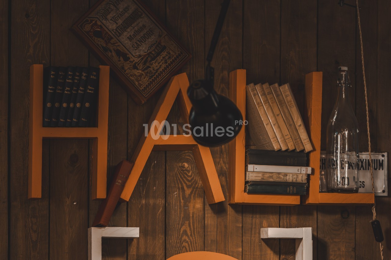 Lettres orange formant le mot ’HALL’ utilisées comme étagères, contenant des livres et des objets décoratifs.