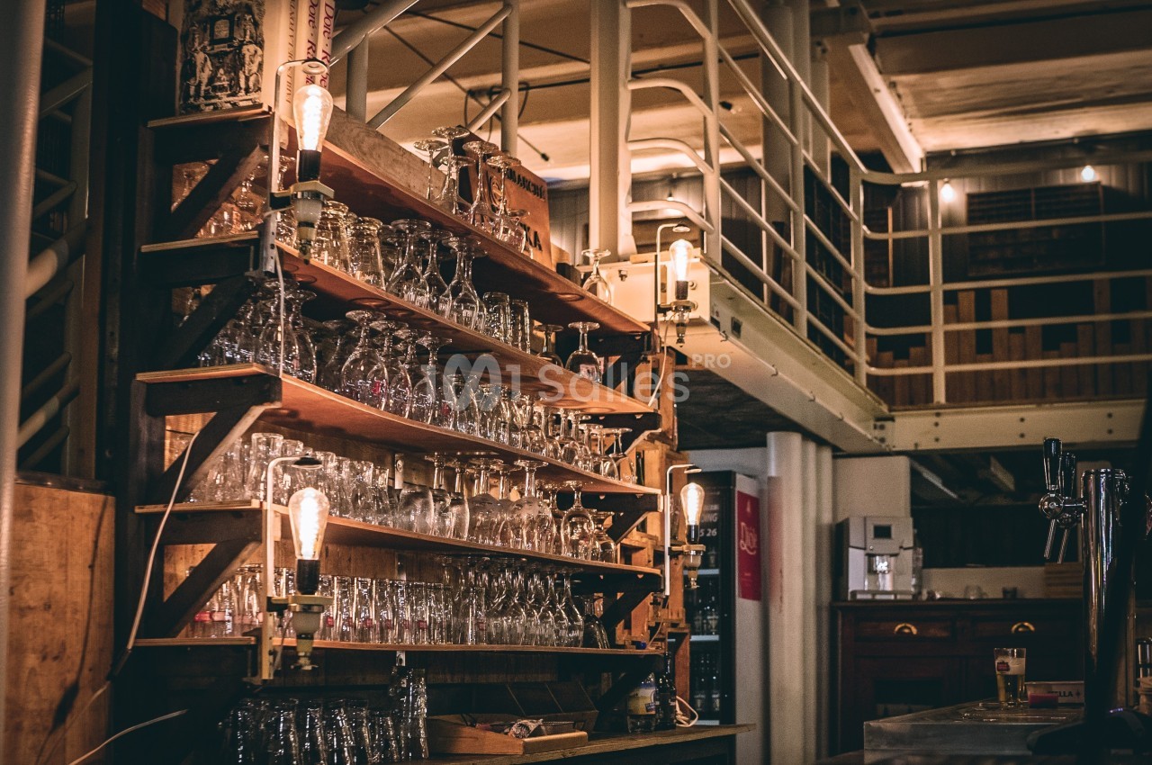 Étagères en bois remplies de verres dans un bar au décor industriel avec éclairage chaleureux.