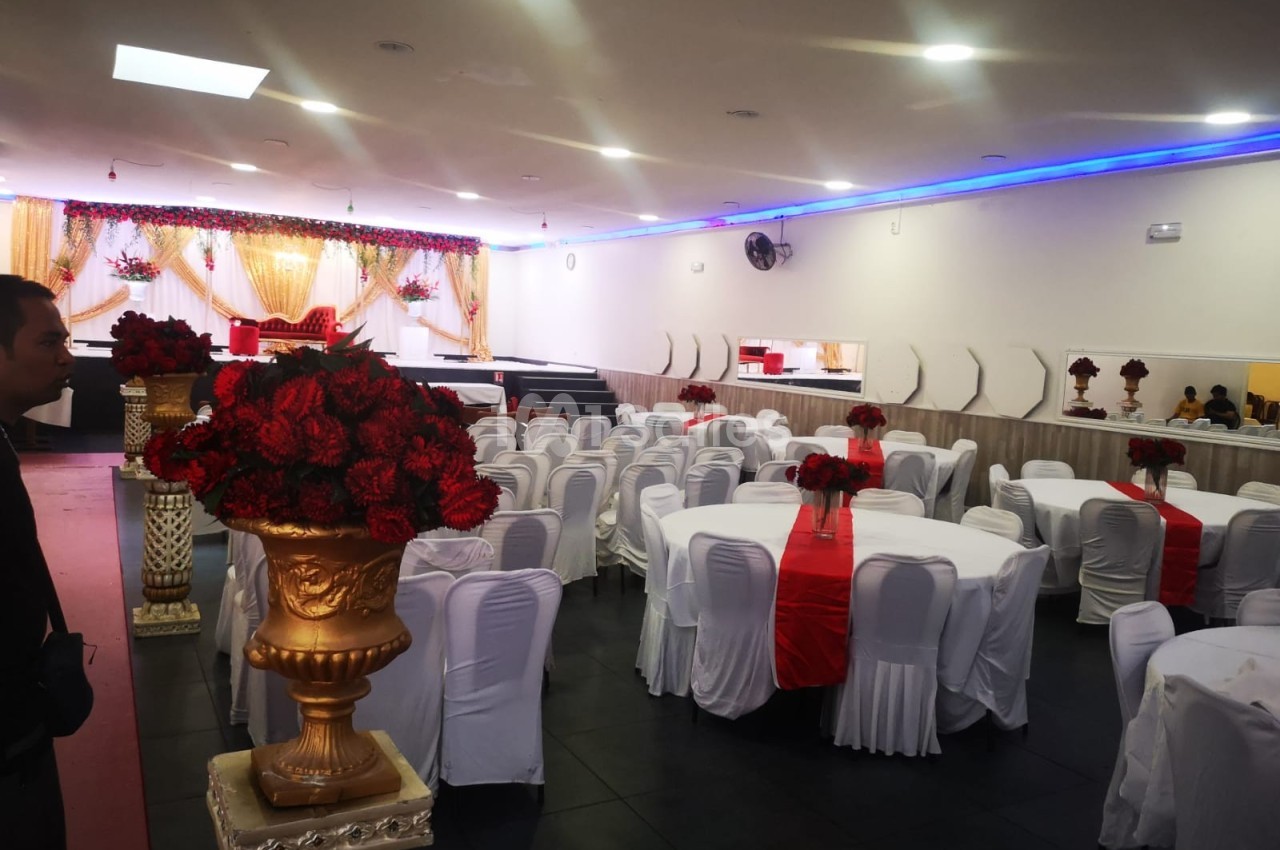 Salle de réception décorée avec des tables rondes, nappes blanches, chemins de table rouges et arrangements floraux rouges.