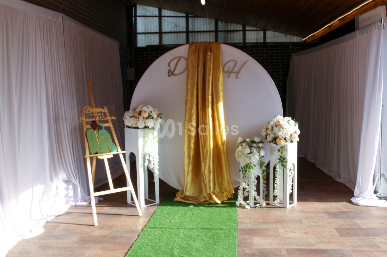 Décor de cérémonie avec un fond circulaire blanc, drapé doré, fleurs blanches et un chevalet de bienvenue.