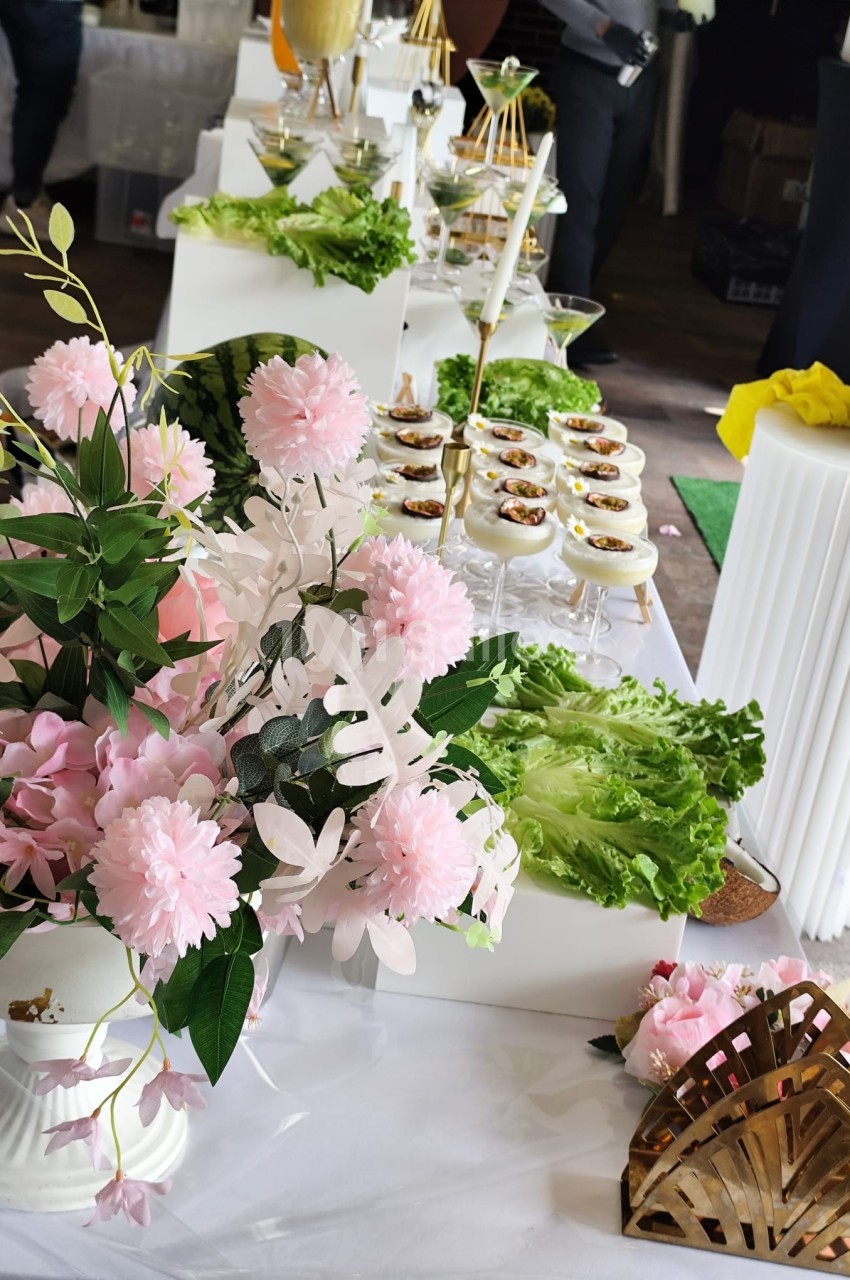 Buffet décoré avec des fleurs roses, des feuilles de laitue et des amuse-bouches disposés sur une table blanche.