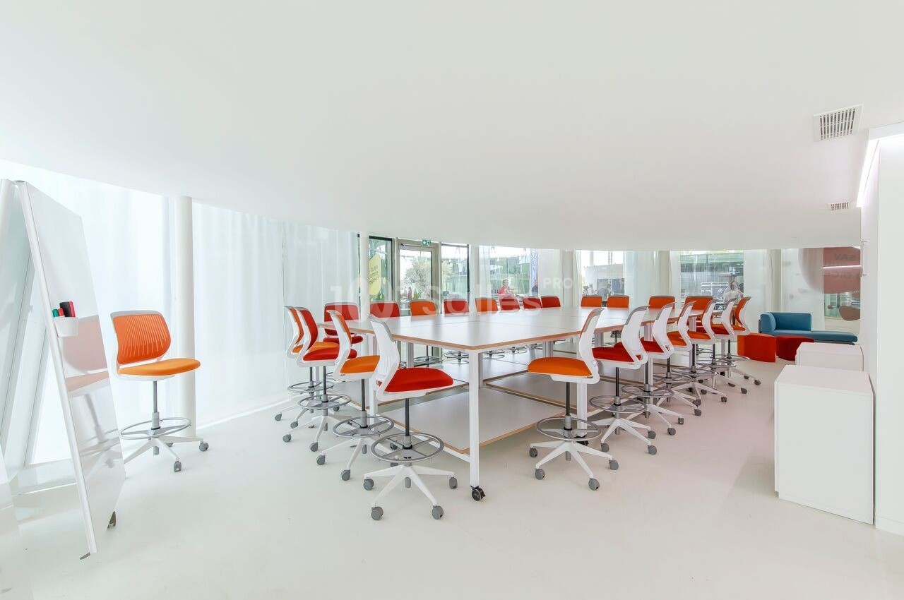 Salle de réunion lumineuse avec une grande table blanche entourée de chaises orange et blanches sur roulettes.