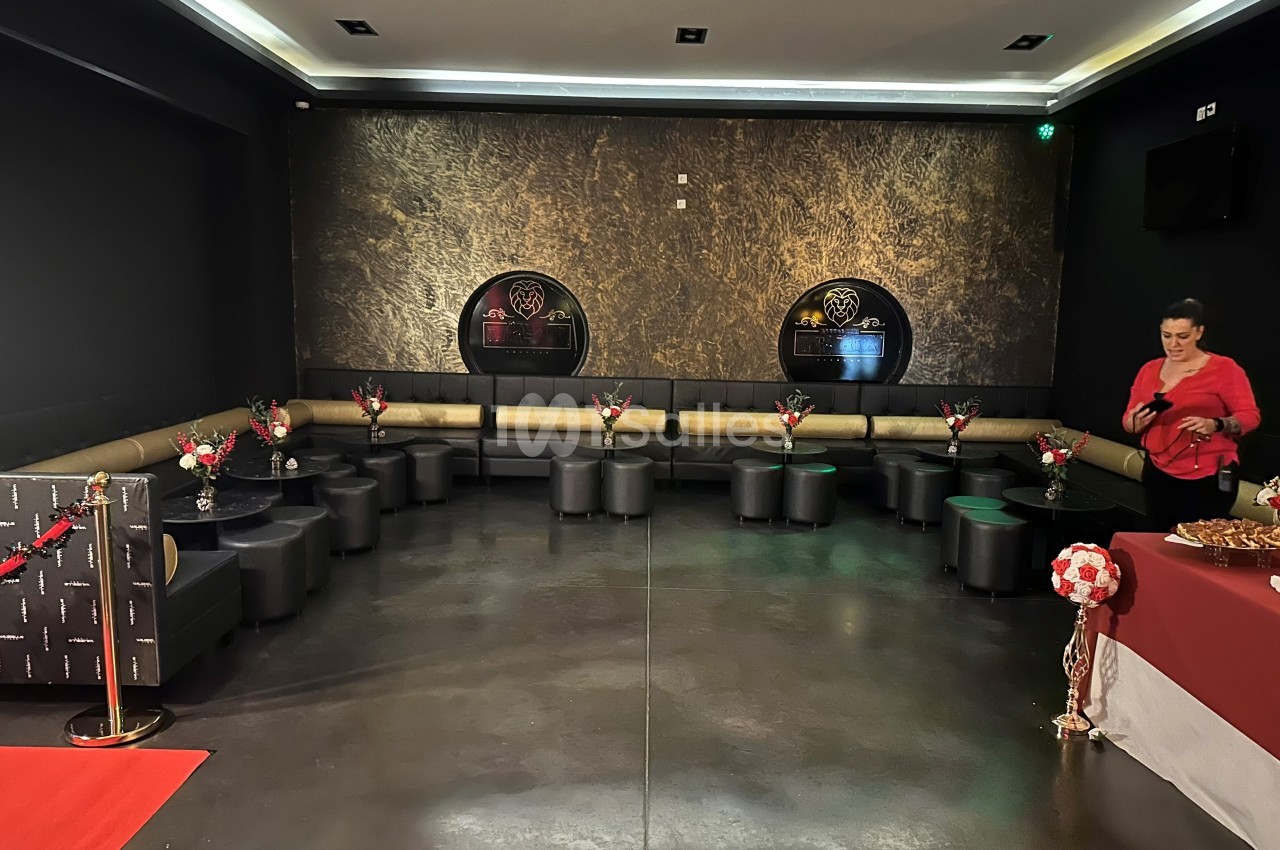 Salle de réception avec banquettes noires, tables basses décorées de fleurs et buffet sur la droite.