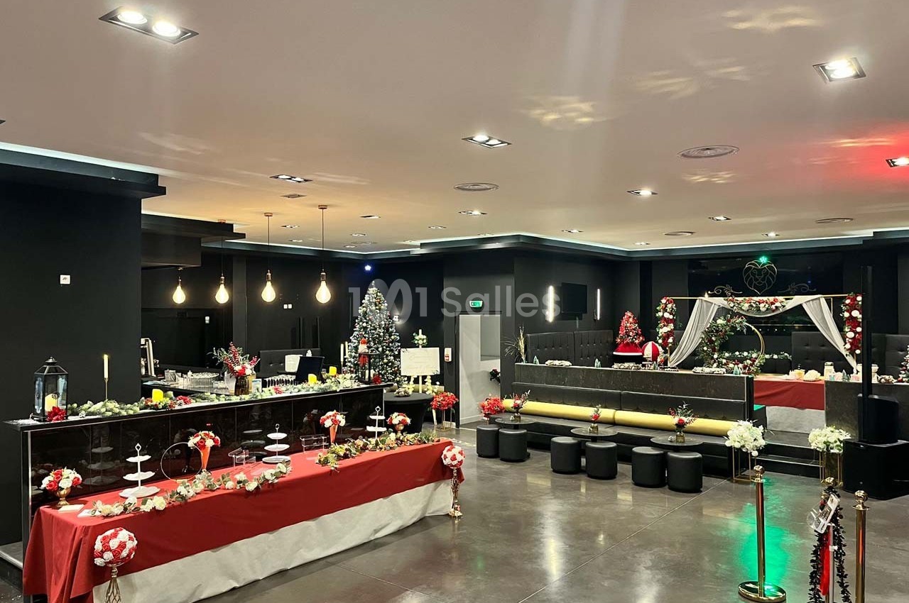 Salle décorée pour les fêtes avec tables dressées, guirlandes lumineuses, sapin de Noël et ornements festifs.