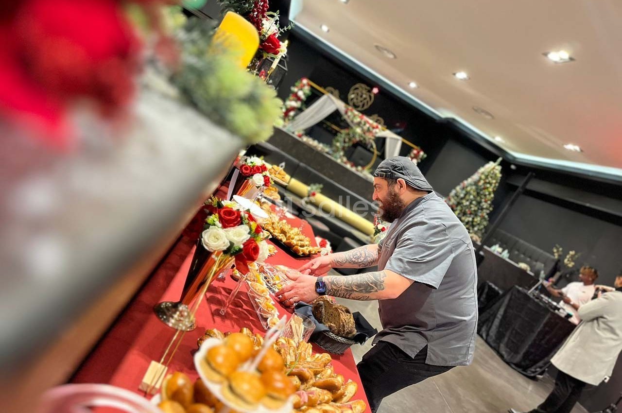 Un chef dispose des plats sur une table décorée de fleurs et de bougies dans une salle festive.