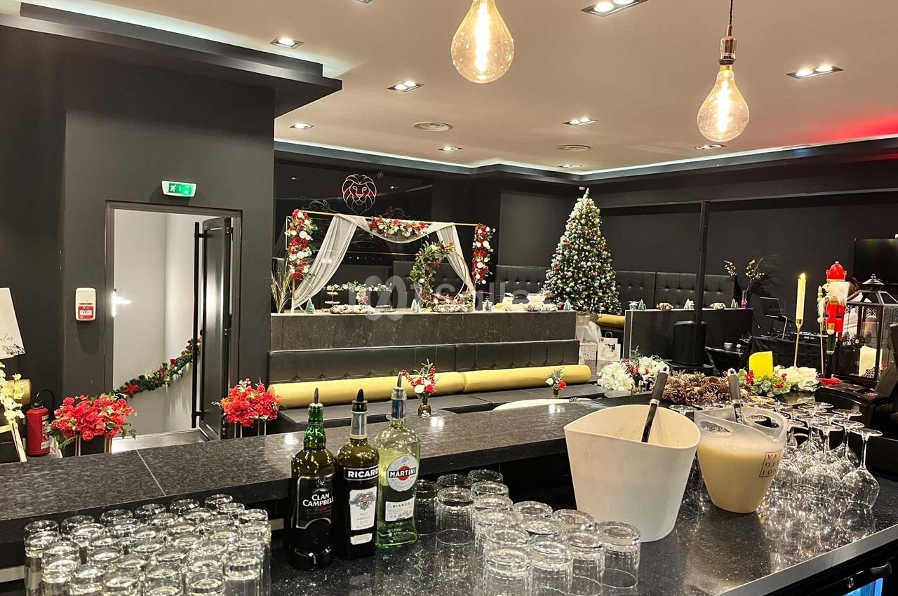 Salle décorée pour les fêtes avec un bar au premier plan, des tables dressées et un sapin de Noël illuminé en arrière-plan.