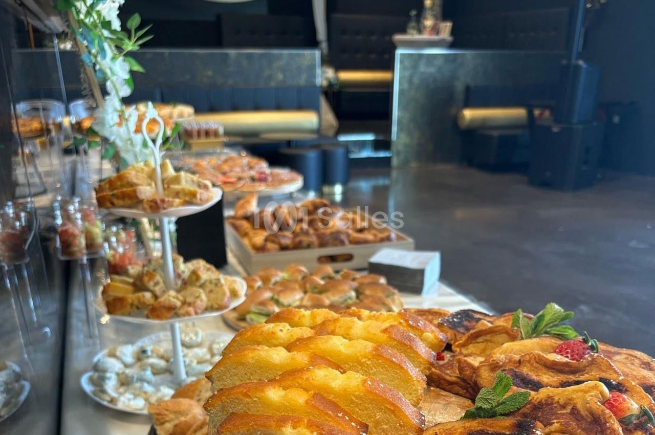 Buffet de pâtisseries et viennoiseries variées disposées sur des présentoirs dans une salle sombre et élégante.