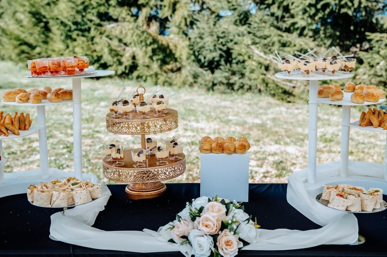 Buffet en plein air avec des amuse-bouches variés disposés sur des présentoirs et une décoration florale au centre.