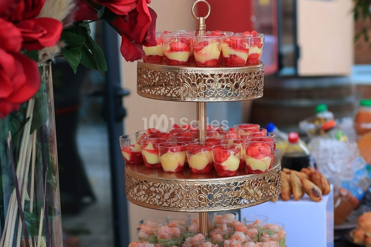 Présentoir doré à deux étages avec verrines de desserts aux fraises et verrines salées, entouré de décorations florales.