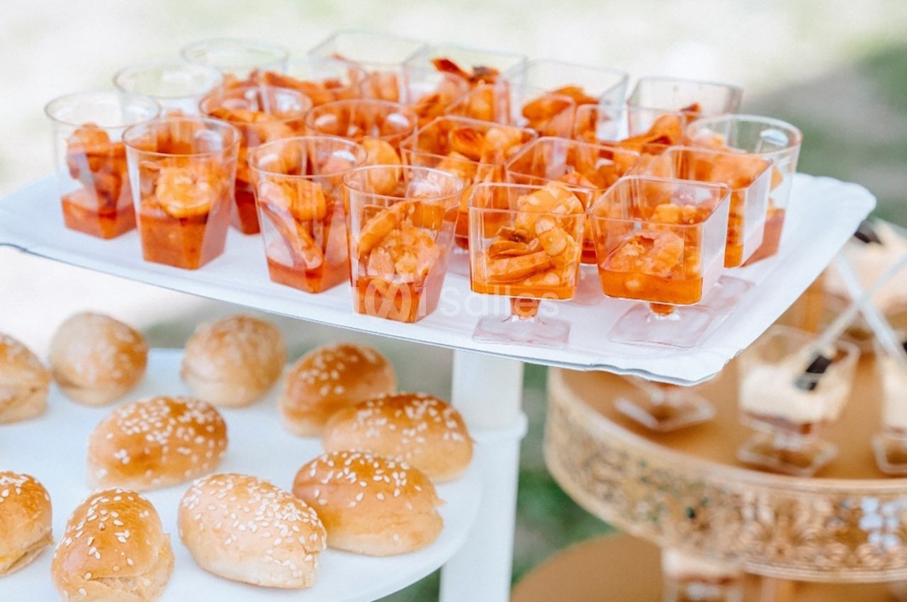 Plateau de verrines de crevettes en sauce et petits pains au sésame disposés sur une table lors d'un buffet.