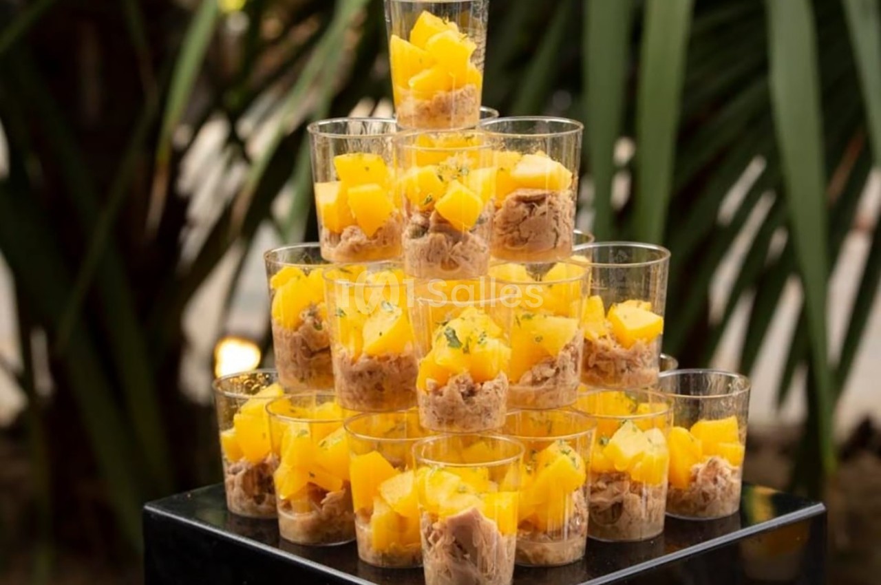 Verrines empilées contenant des morceaux de mangue et une préparation à base de thon, décorées de fines herbes.