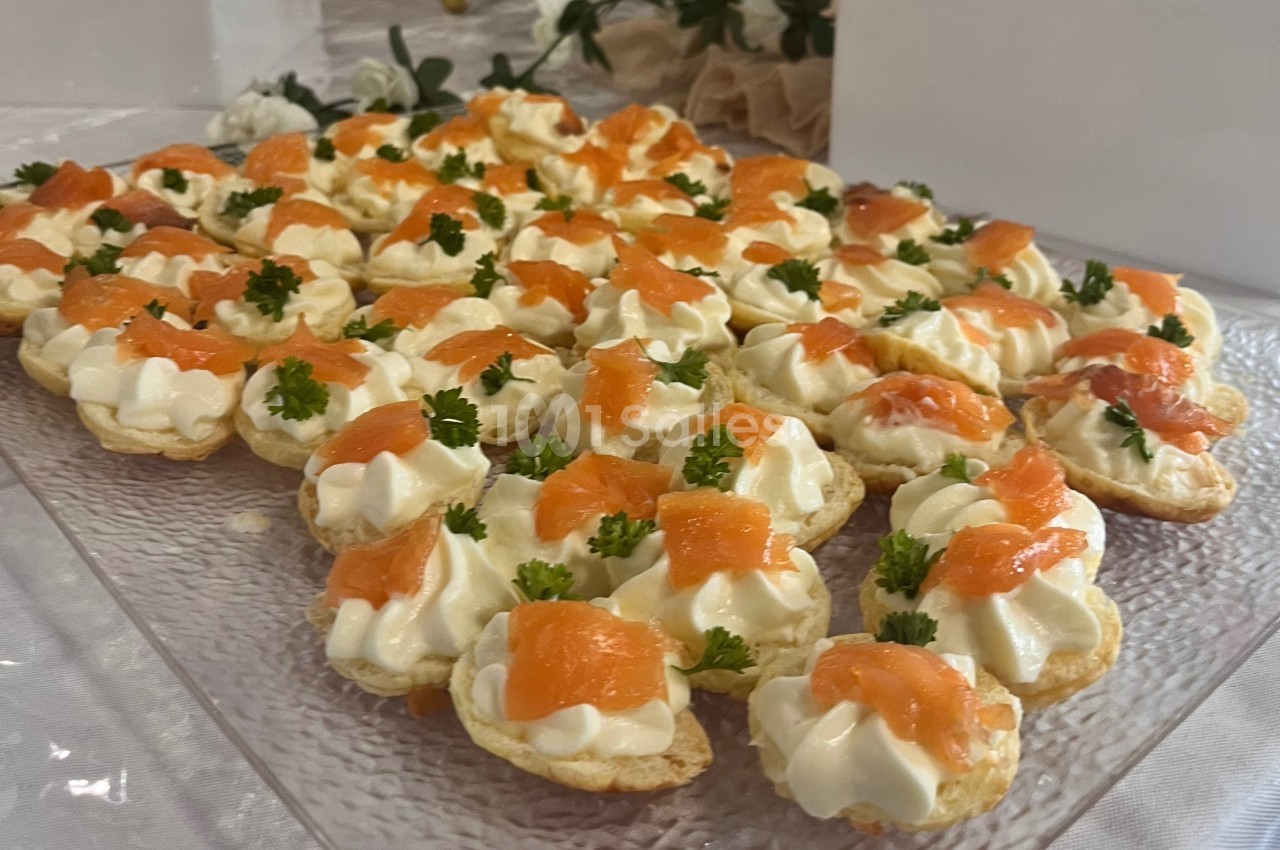 Plateau de canapés au saumon fumé, garnis de crème et décorés de brins de persil sur une table dressée.