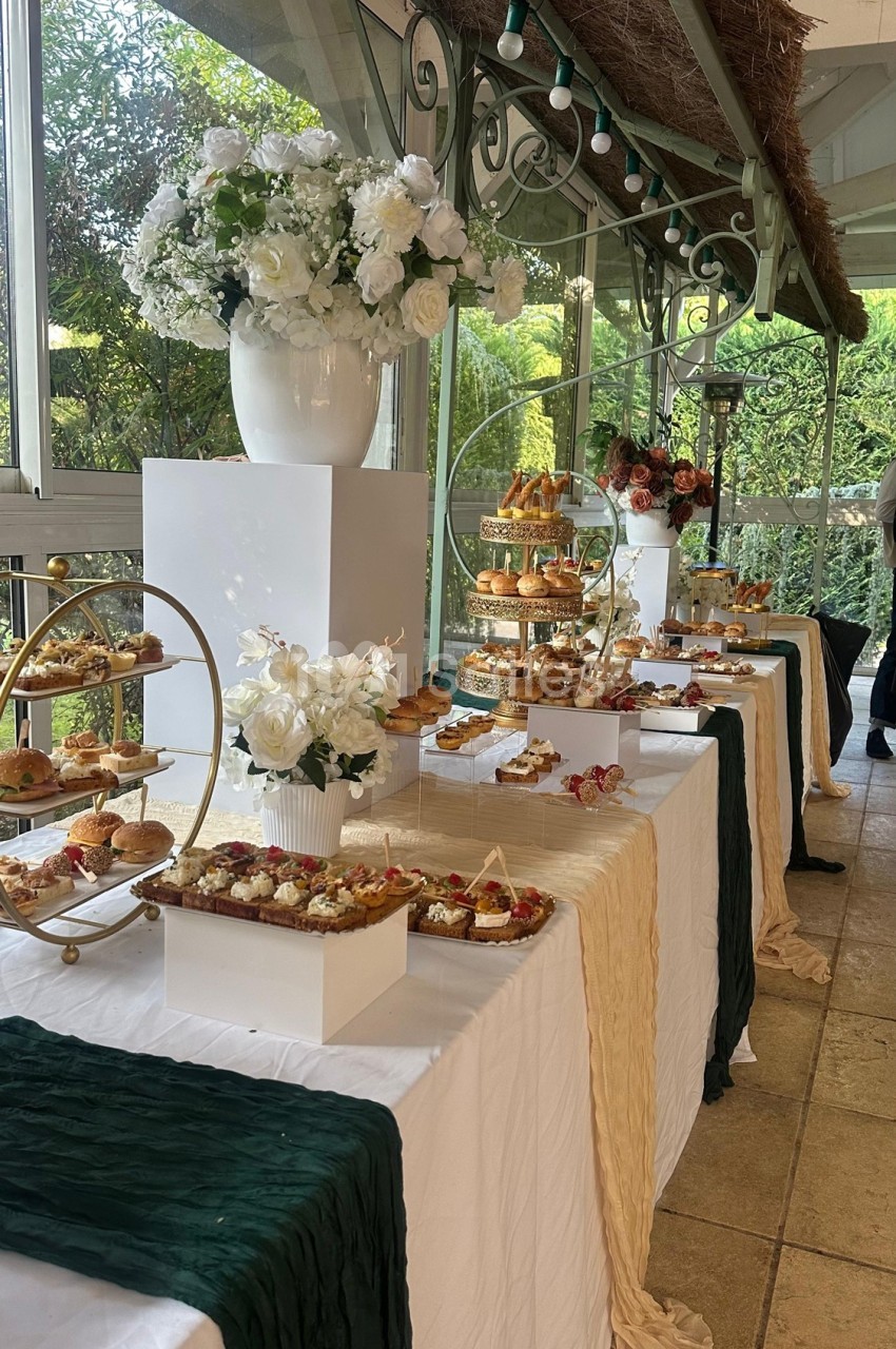 Table garnie de pâtisseries variées, présentées sur des supports élégants, avec des fleurs blanches en décoration.