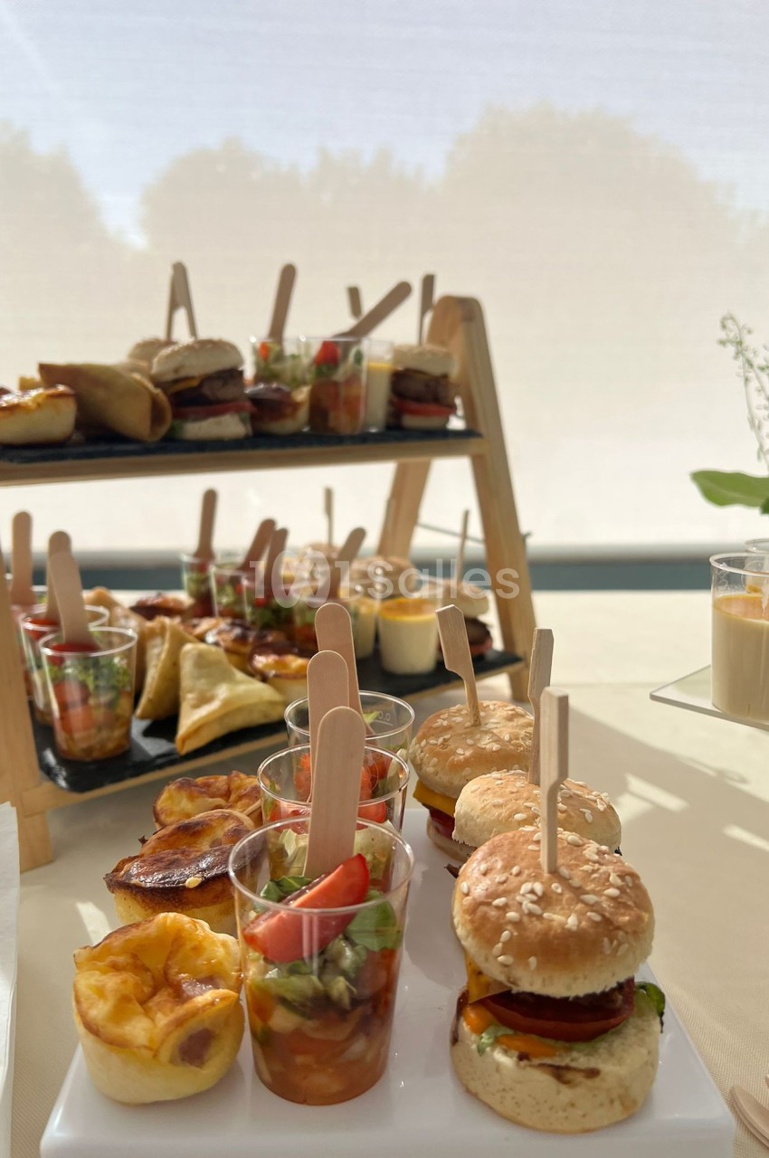 Plateau de mini-burgers, verrines et amuse-bouches variés disposés sur une table lumineuse.
