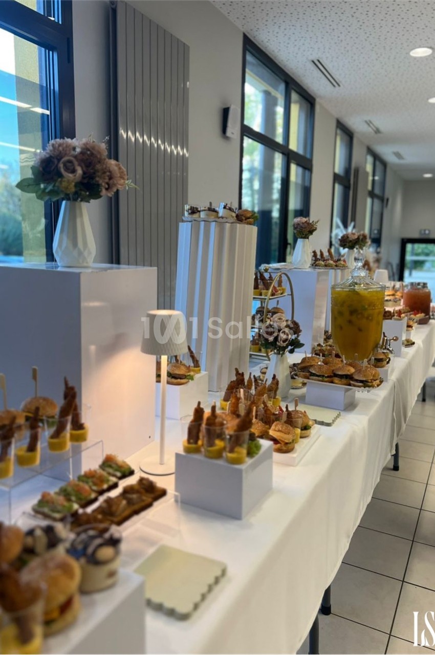 Buffet élégant avec verrines, amuse-bouches et boissons disposés sur des tables blanches dans une salle lumineuse.