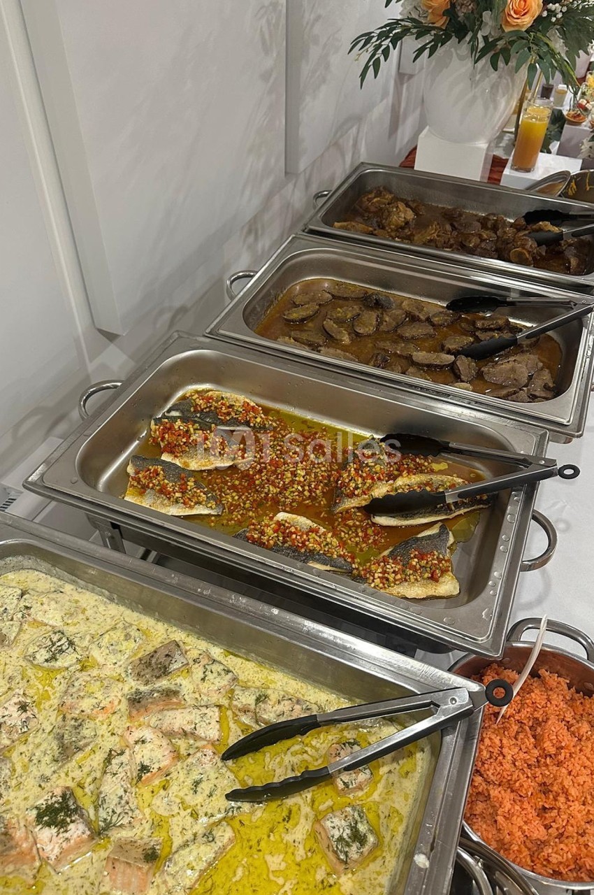 Buffet avec plats variés comprenant poissons en sauce, viande en sauce brune et riz coloré, disposés dans des plats en inox.