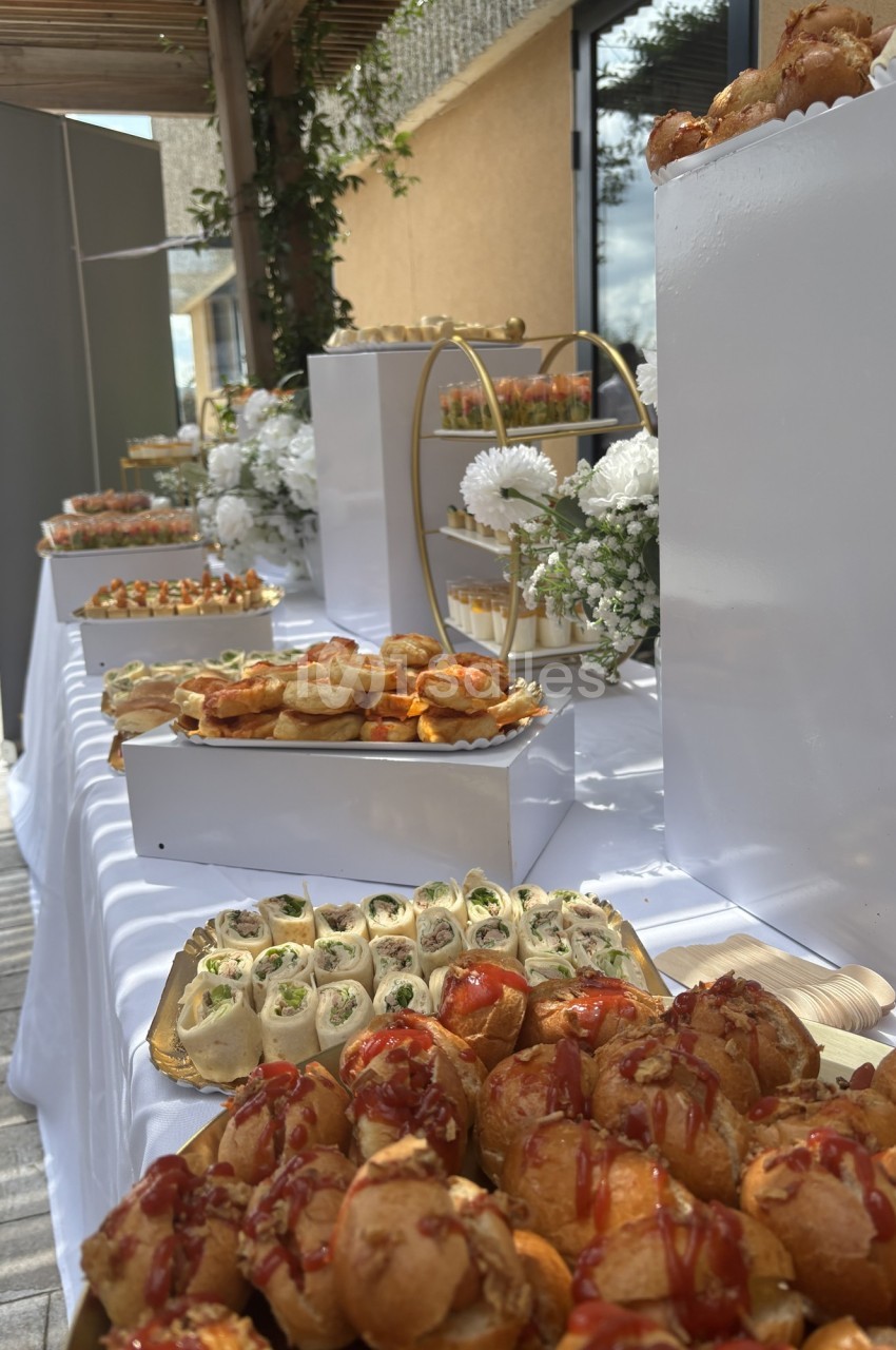 Buffet extérieur avec divers amuse-bouches, dont des choux garnis, wraps et verrines, décoré de fleurs blanches.