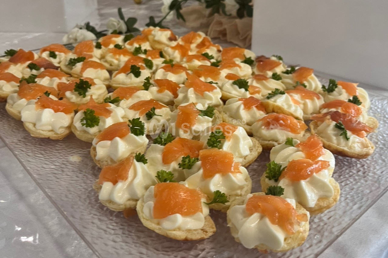Plateau de canapés au saumon fumé, garnis de crème et décorés de brins de persil sur une table dressée.