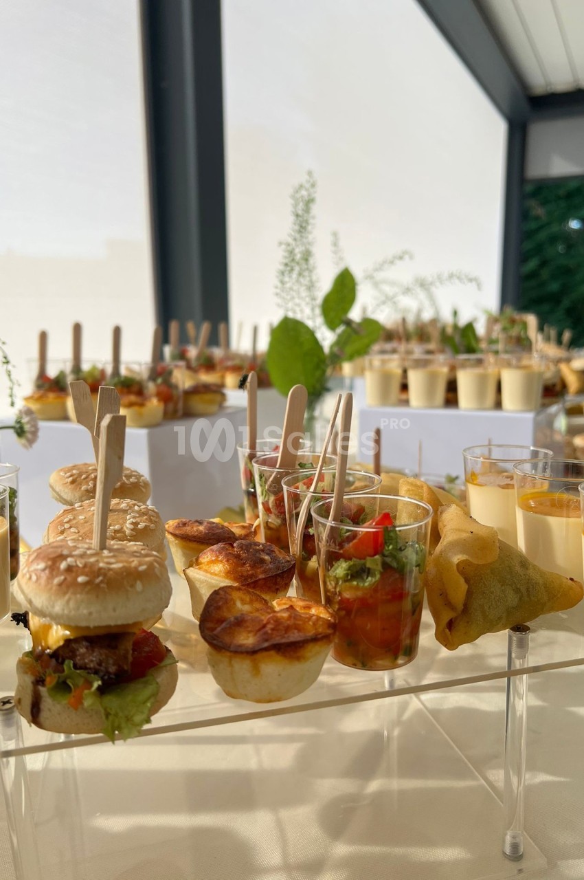 Buffet avec mini-burgers, verrines, samoussas et autres amuse-bouches disposés sur une table lumineuse.