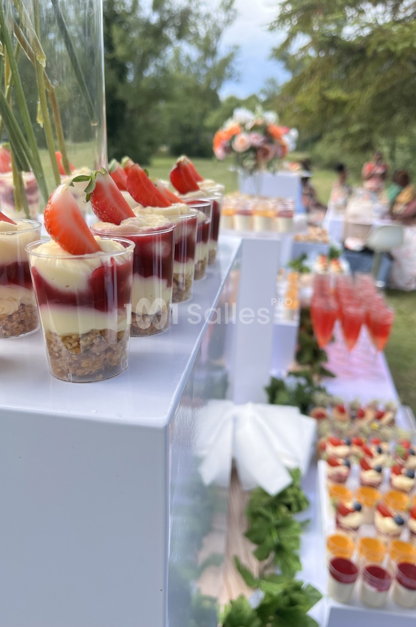 Desserts en verrines avec fraises et mousse, disposés sur une table extérieure décorée pour un événement.