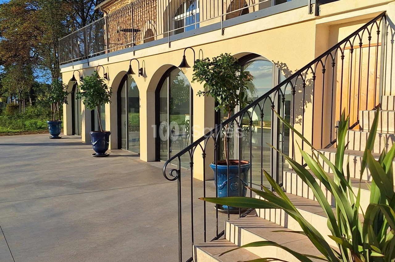 Façade ensoleillée d'un bâtiment avec arches vitrées, pots de fleurs bleus et escalier en premier plan.