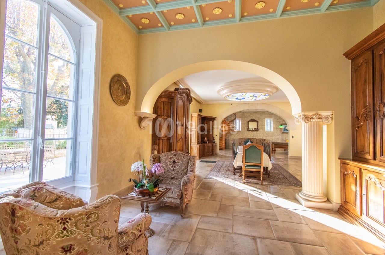 Salle à manger lumineuse avec mobilier en bois, voûtes, colonnes décoratives et vue sur un jardin par une grande fenêtre.