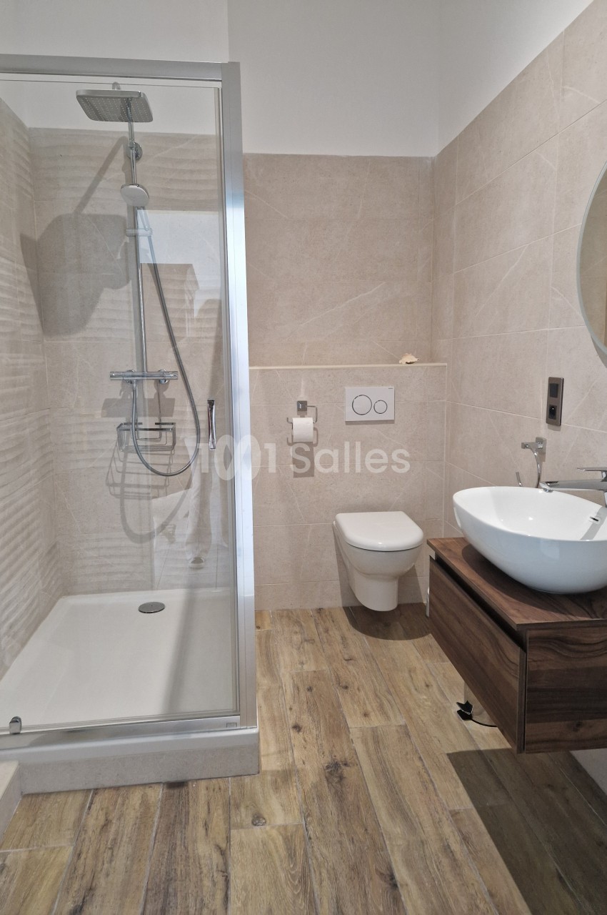 Salle de bain moderne avec douche à l'italienne, lavabo sur meuble en bois, toilettes suspendues et miroir rond.