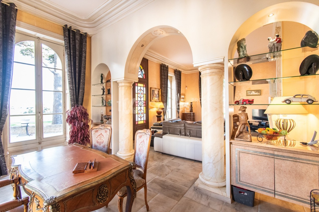 Salle de séjour lumineuse avec arches, mobilier classique, étagères décoratives et vue sur un jardin à travers une grande…