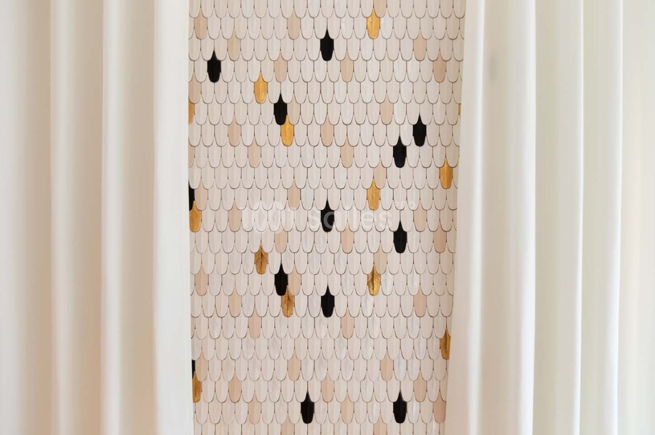 Motif mural en écailles beige, noir et doré, encadré par des rideaux blancs.