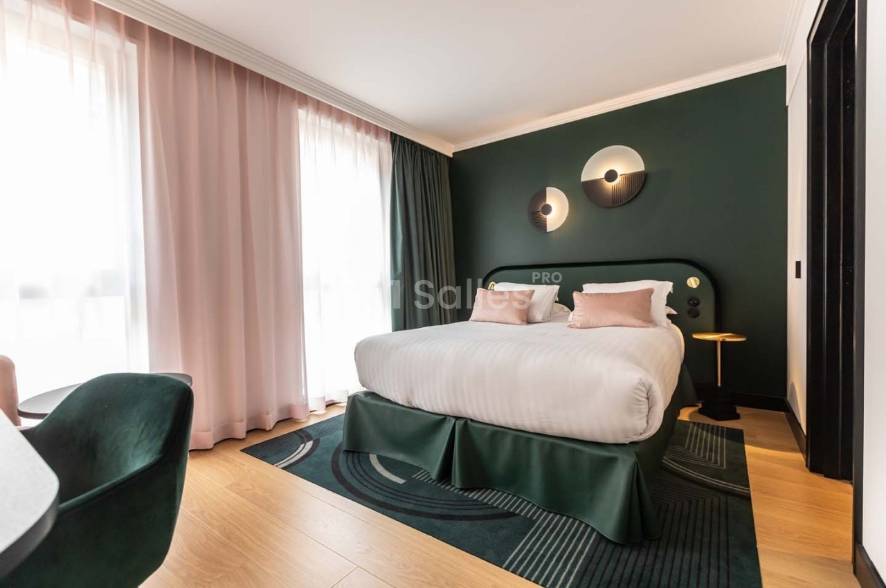 Chambre moderne avec lit double, murs vert foncé, rideaux roses, parquet clair et éclairage design.
