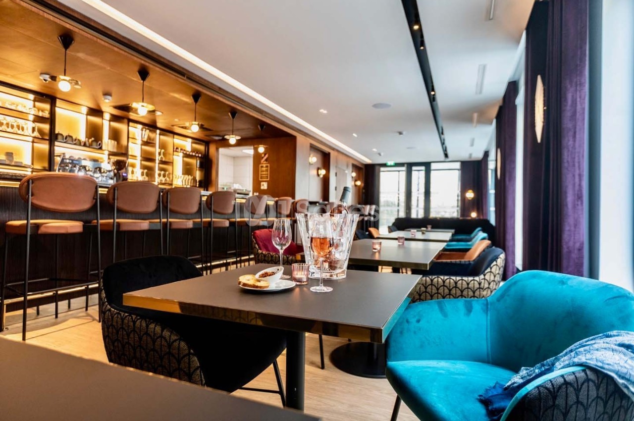 Salle de restaurant moderne avec bar en arrière-plan, tables dressées et fauteuils colorés.