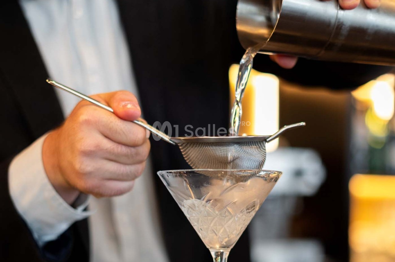 Un barman verse un cocktail filtré dans un verre à martini rempli de glace.