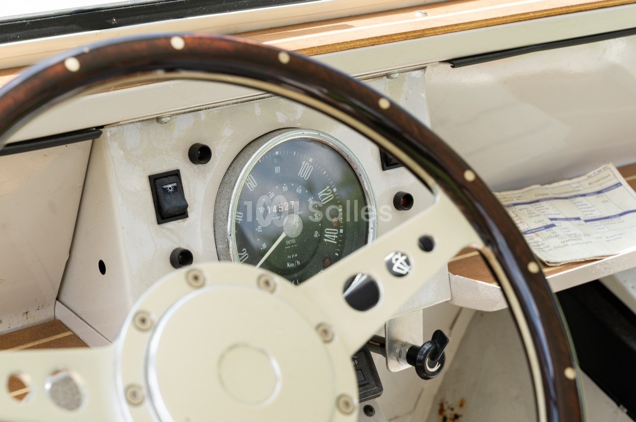 Volant en bois et tableau de bord d'un bateau avec un compteur et un document posé à côté.