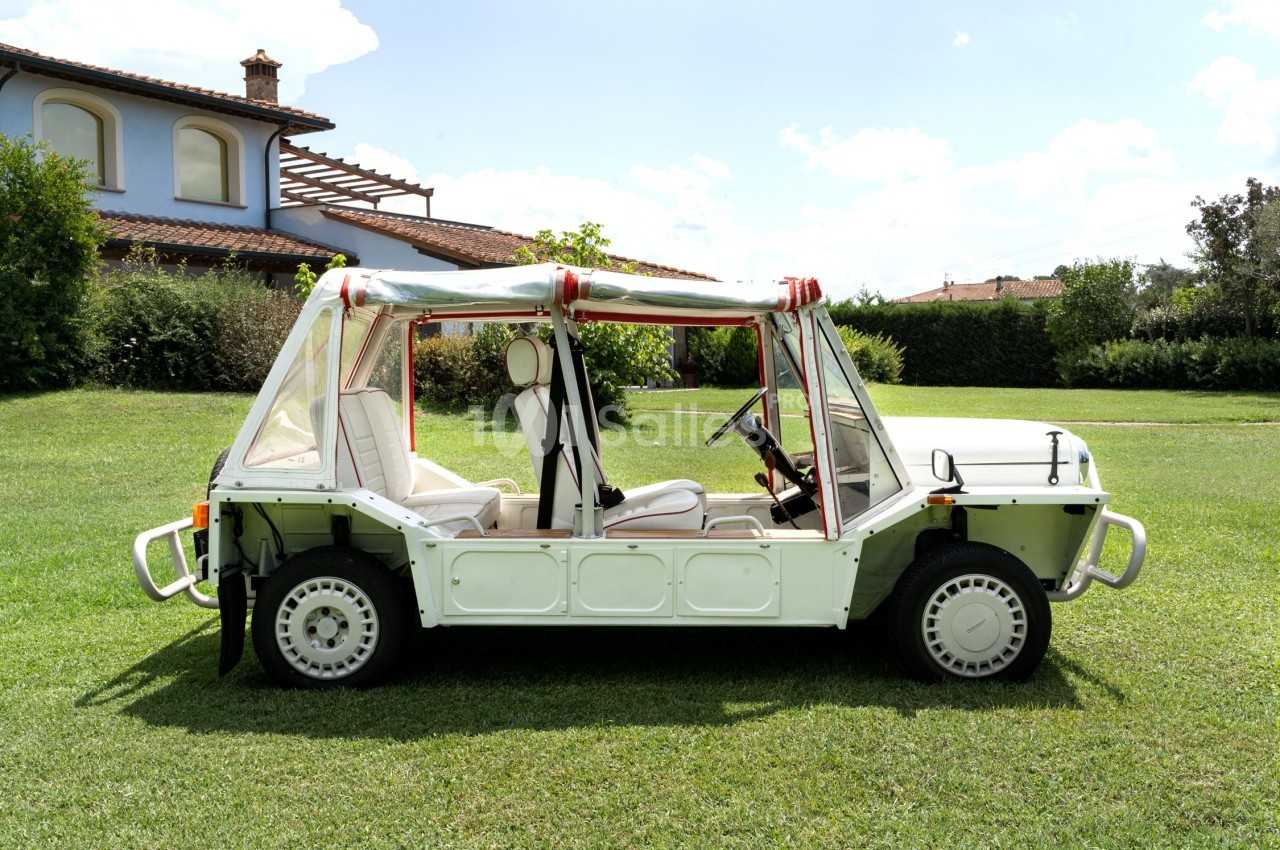 Voiture blanche décapotable stationnée sur une pelouse, avec une maison en arrière-plan.