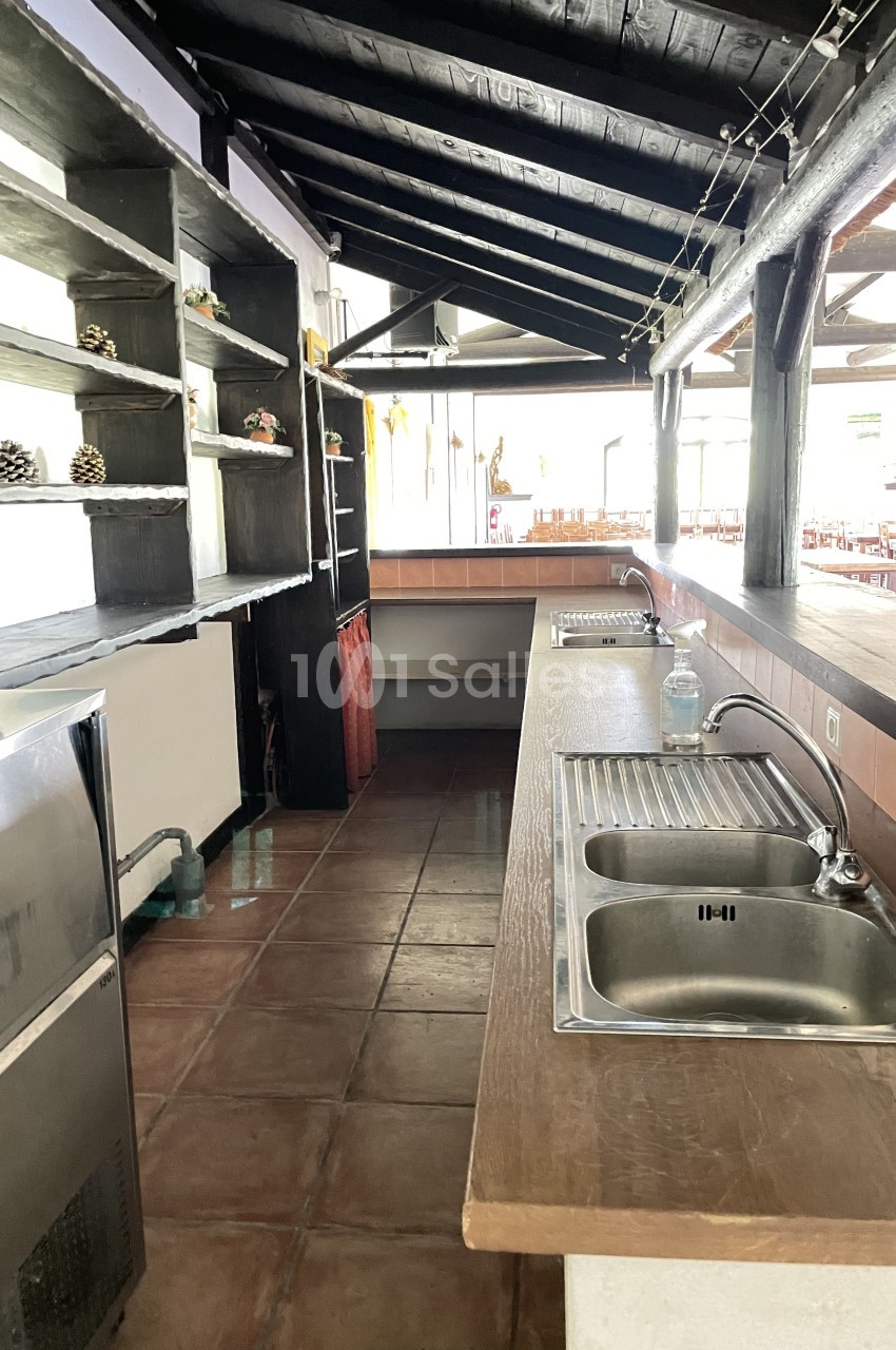 Cuisine ouverte avec plan de travail en bois, double évier en inox, étagères murales et carrelage au sol.