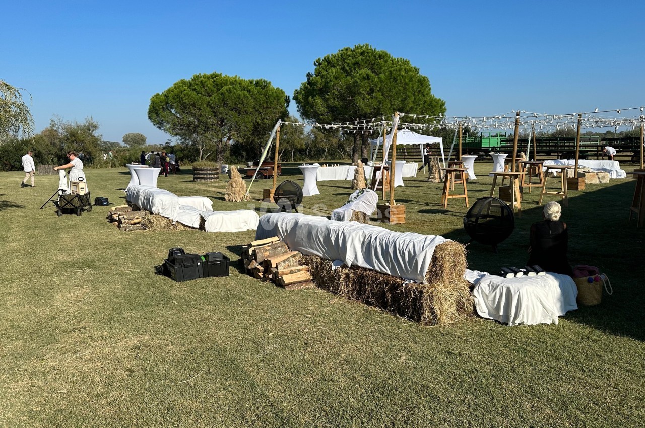Espace extérieur aménagé avec bottes de foin recouvertes de tissus blancs, tables hautes et guirlandes lumineuses.