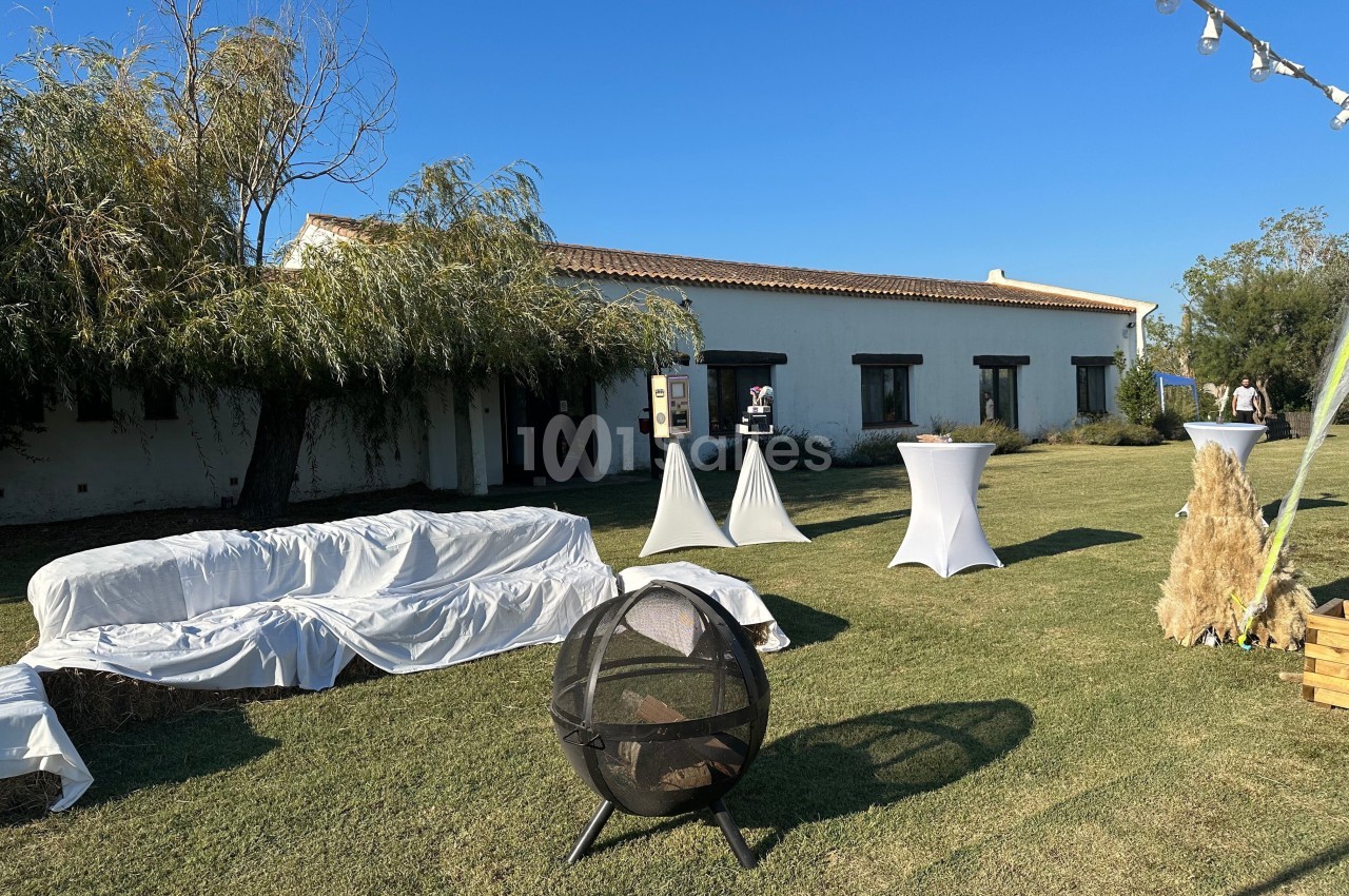 Espace extérieur avec pelouse, mobilier de réception, bâtiment blanc en arrière-plan et ciel dégagé.