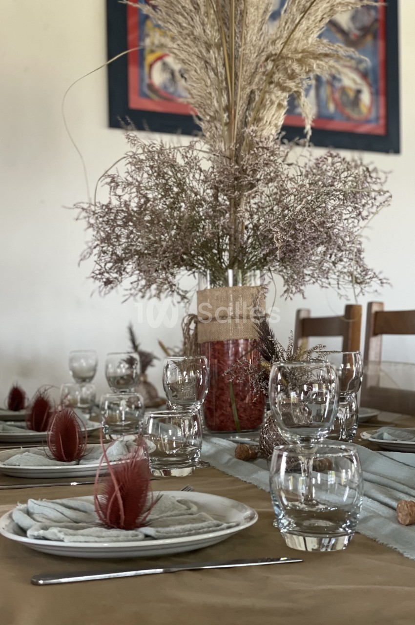 Table dressée avec des assiettes, verres et serviettes, décorée de plumes rouges et d'un bouquet de fleurs séchées.
