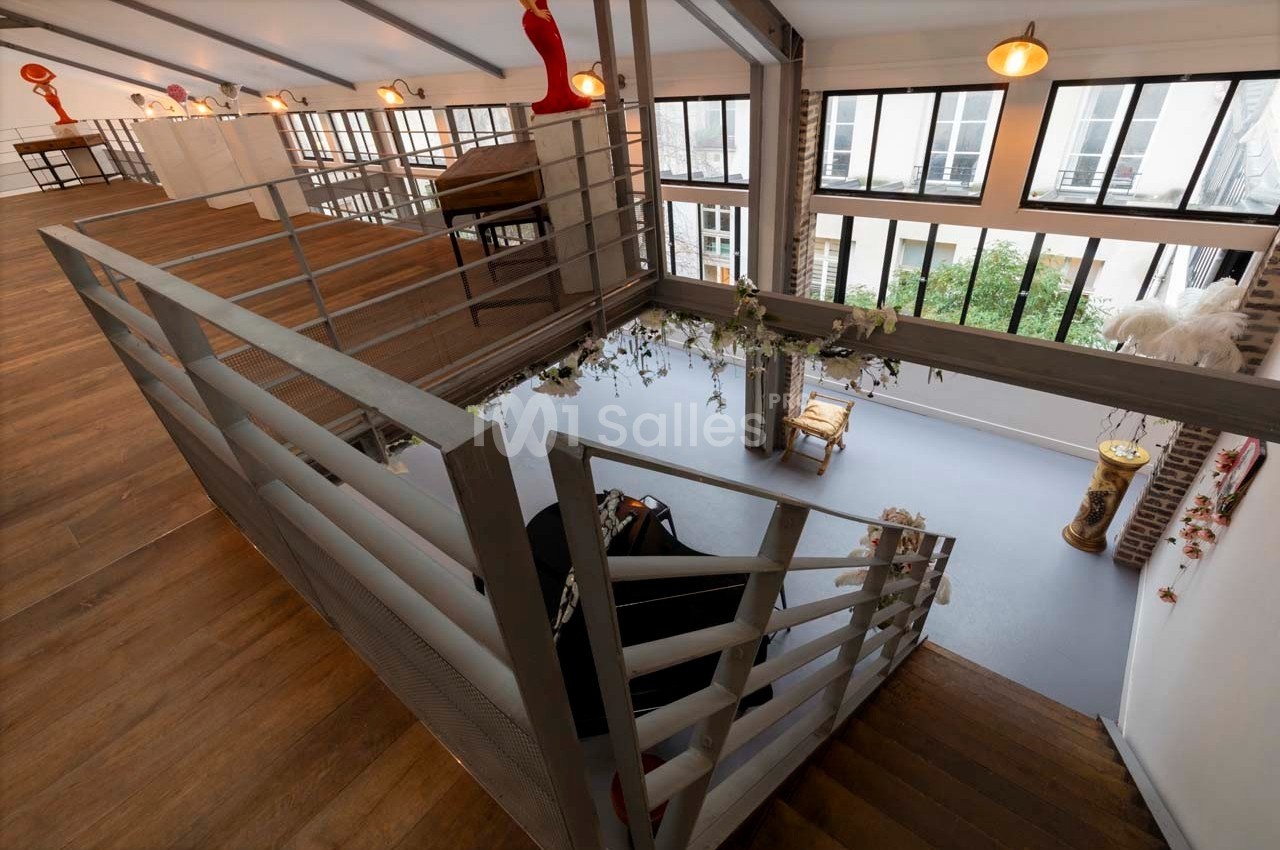 Escalier en bois et métal menant à un espace lumineux avec de grandes fenêtres et un piano au rez-de-chaussée.