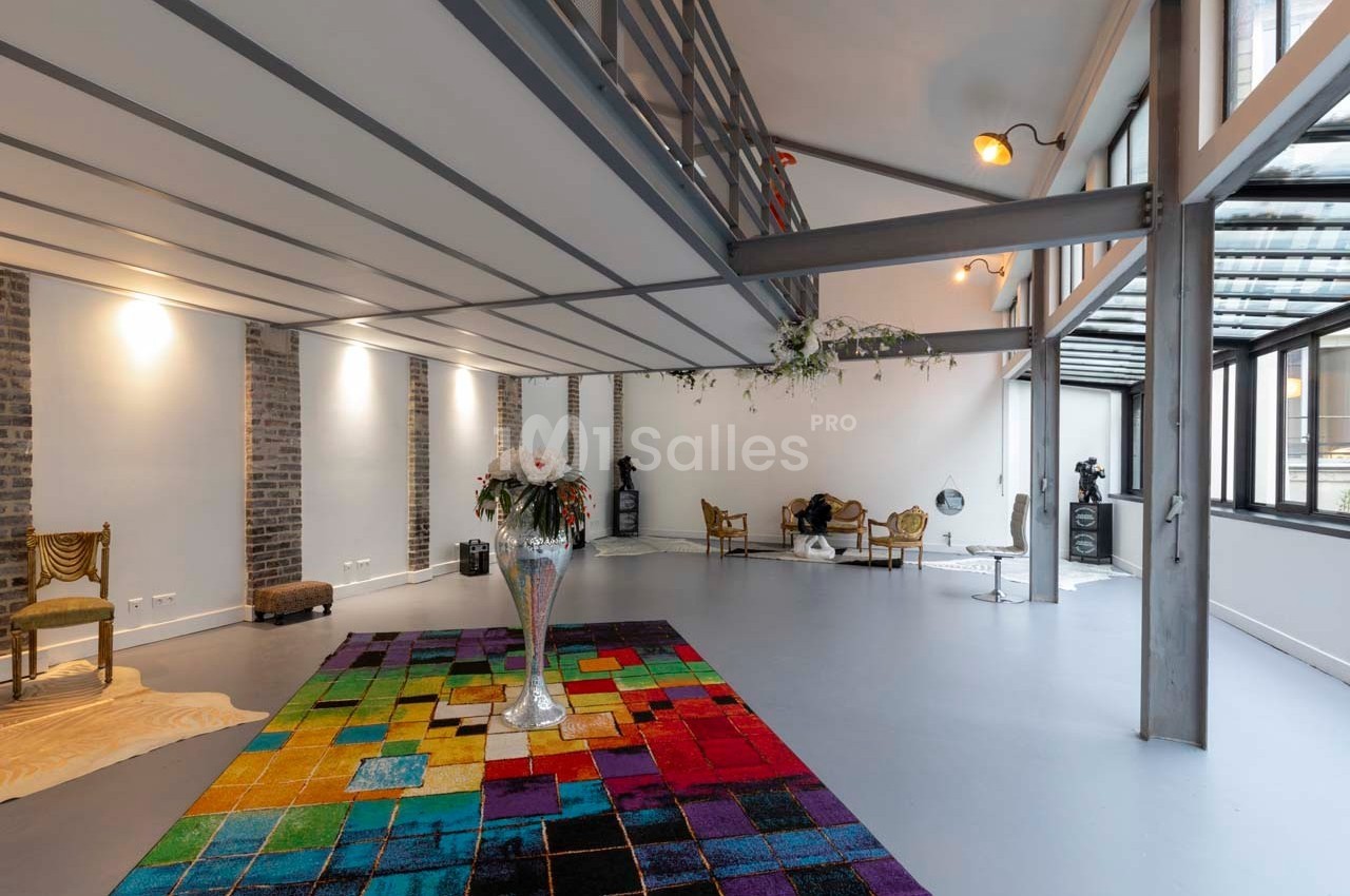 Espace intérieur lumineux avec un sol gris, un tapis coloré, des meubles éclectiques et une grande baie vitrée.